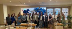 Line-up of smartly dressed people standing in front of big bunch of balloons posing for photo to celebrate 20-year anniversary
