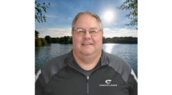 Headshot of a man smiling to the camera with a calm lake in the background.