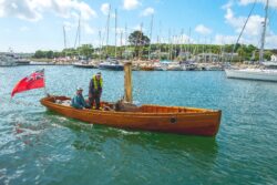 wooden steam boat with two people onboard and a red ensign flying