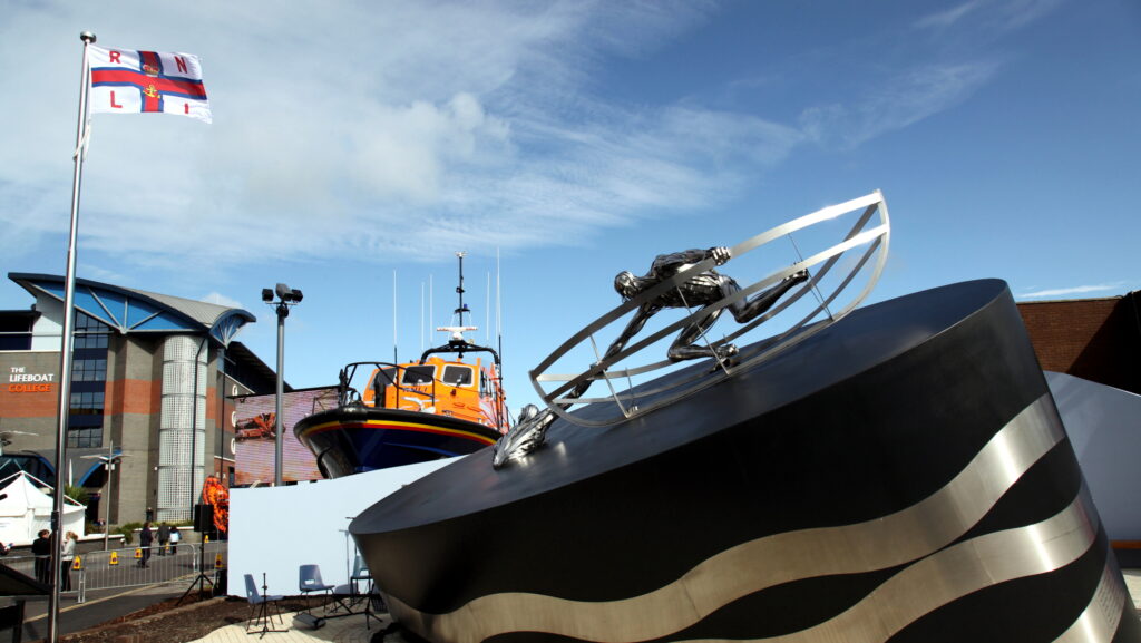 RNLI memorial ceremony. Picture shows the memorial with the Lifeboat College behind. Poole. Flag