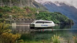 Small white ferry uplifted out of water on red foils with cloud covered mountains in background of still, reflective lake