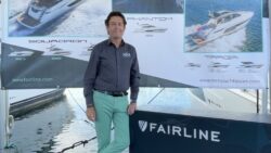 dark hair man standing by Fairline sign and stand