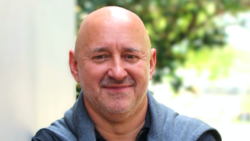 A man looks at the camera. He has a jumper draped around his shoulders.