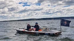 Two rowers in a boat with a flag.