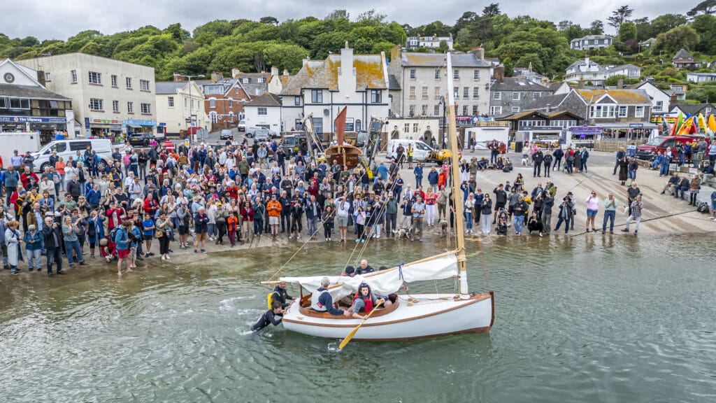 traditional small launch boat in harbour with  a small crowd on harbour front