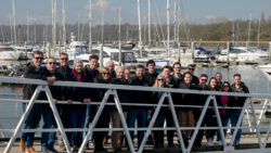 group of people in winter jackets standing on gangway with marina in background