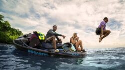 Couple on back of stationary Seadoo jet ski with younger girl jumping into the water in mid air